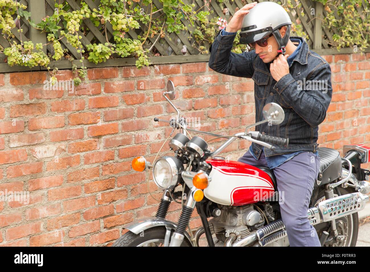 Mid adult man, sitting on motorbike, putting on helmet Stock Photo