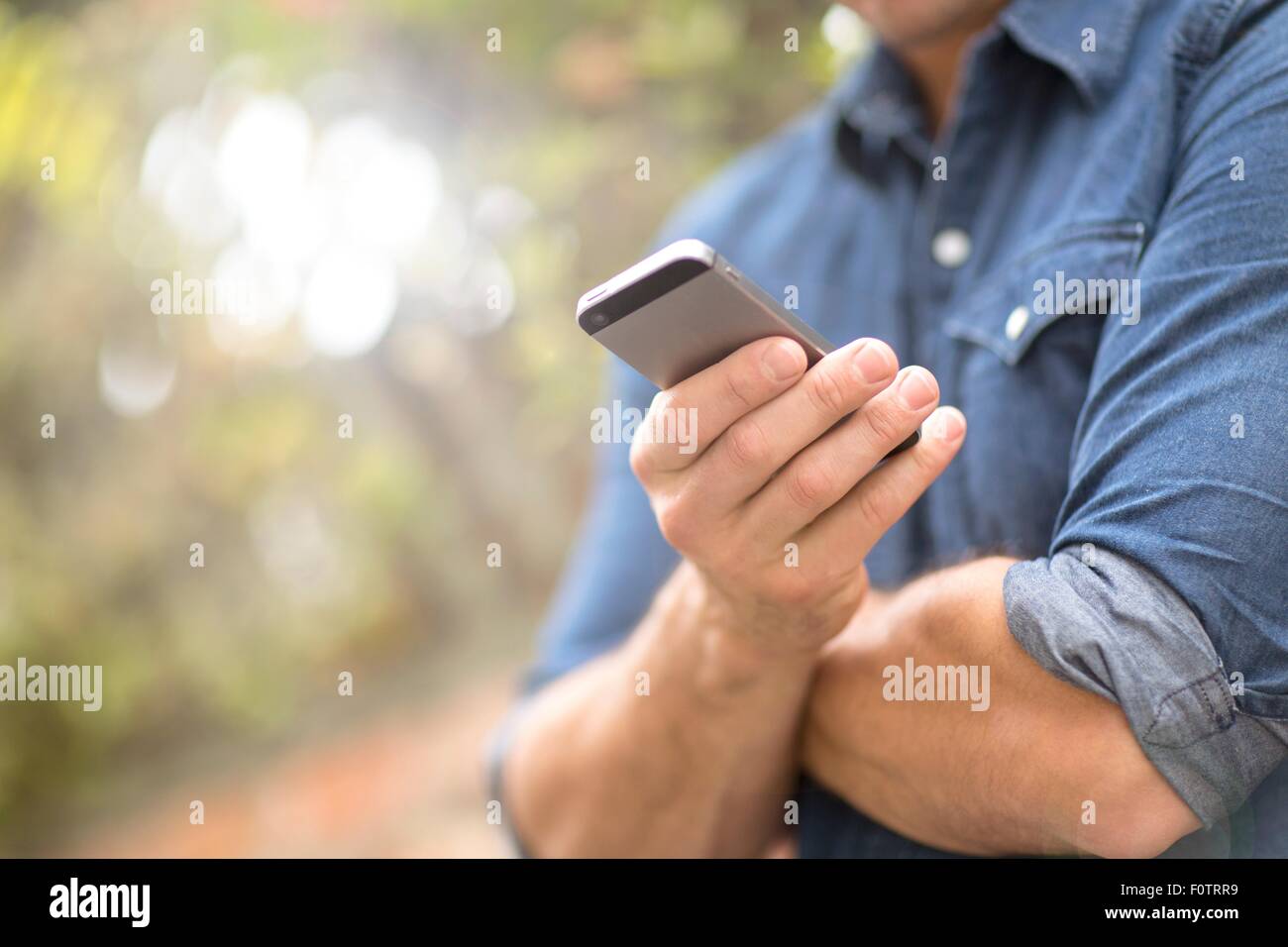 Mid adult man, outdoors, using mobile phone, mid section Stock Photo