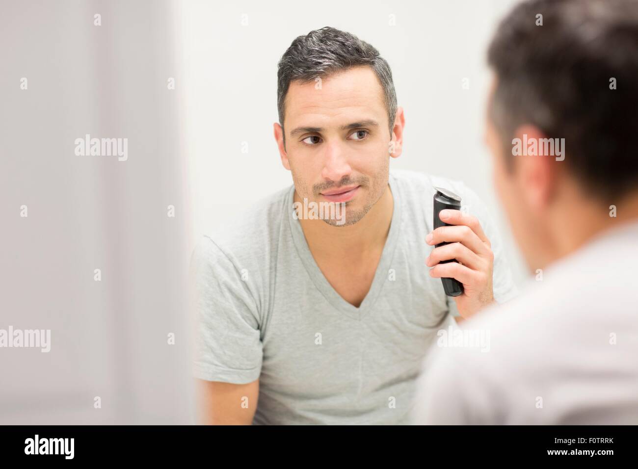 Mid adult man, looking in mirror, using electric shaver Stock Photo