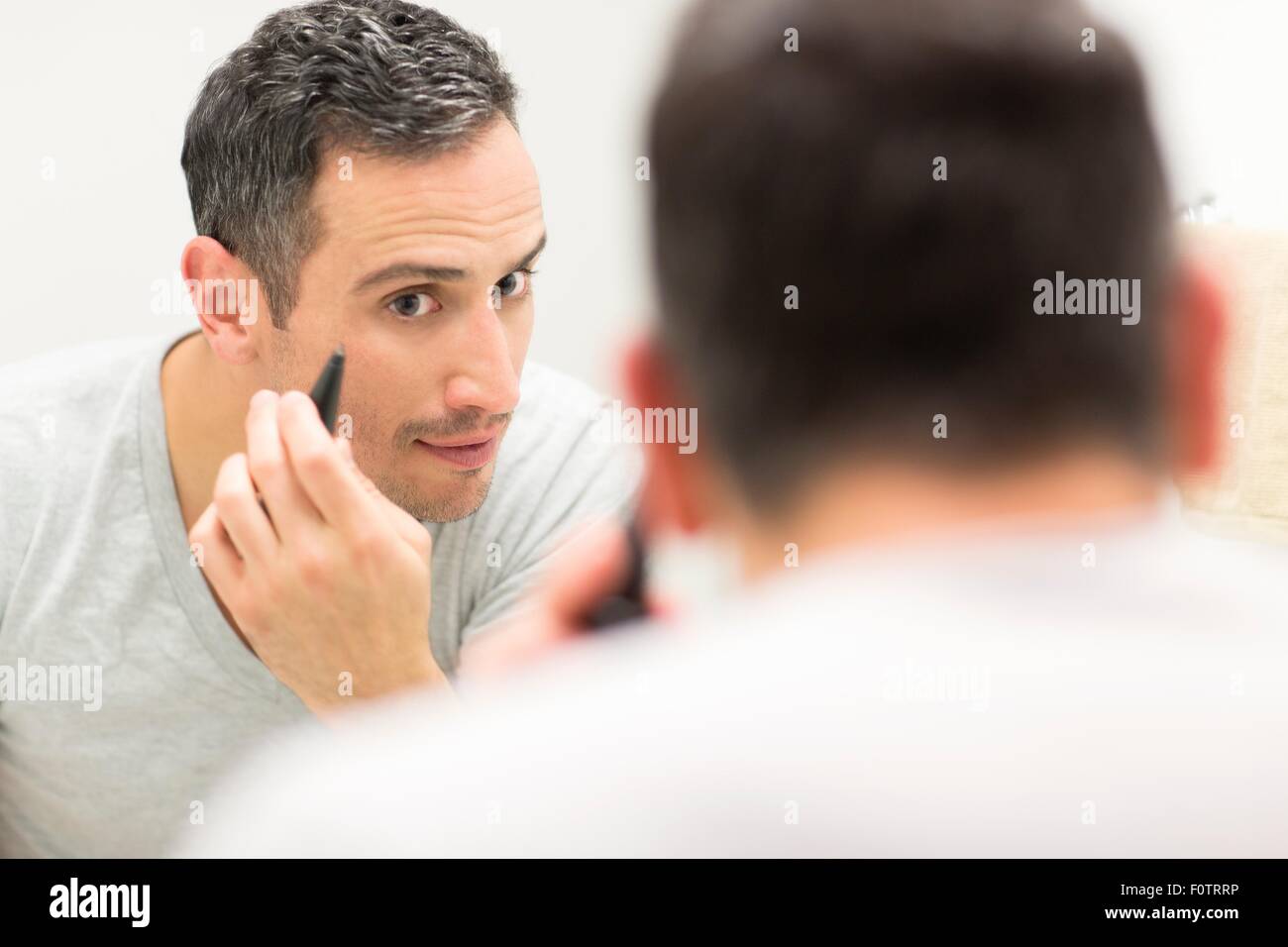 Mid adult man, looking in mirror, using tweezers, rear view Stock Photo