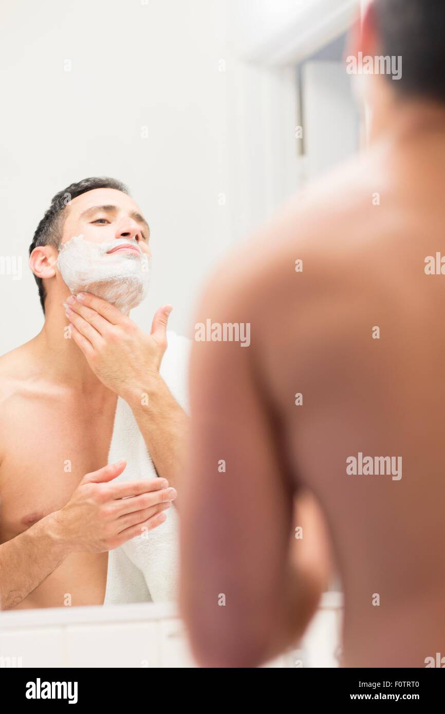 Mid adult man, looking in mirror, applying shaving foam to neck, rear view Stock Photo