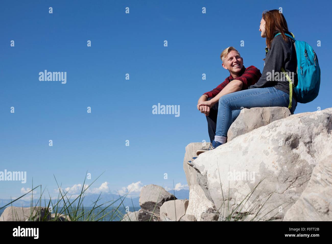 Low angle view of young couple sitting on rocks smiling Stock Photo