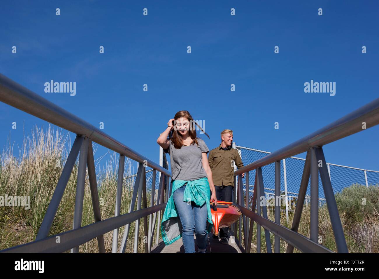 Front view of young couple carrying kayak on walkway with railings Stock Photo