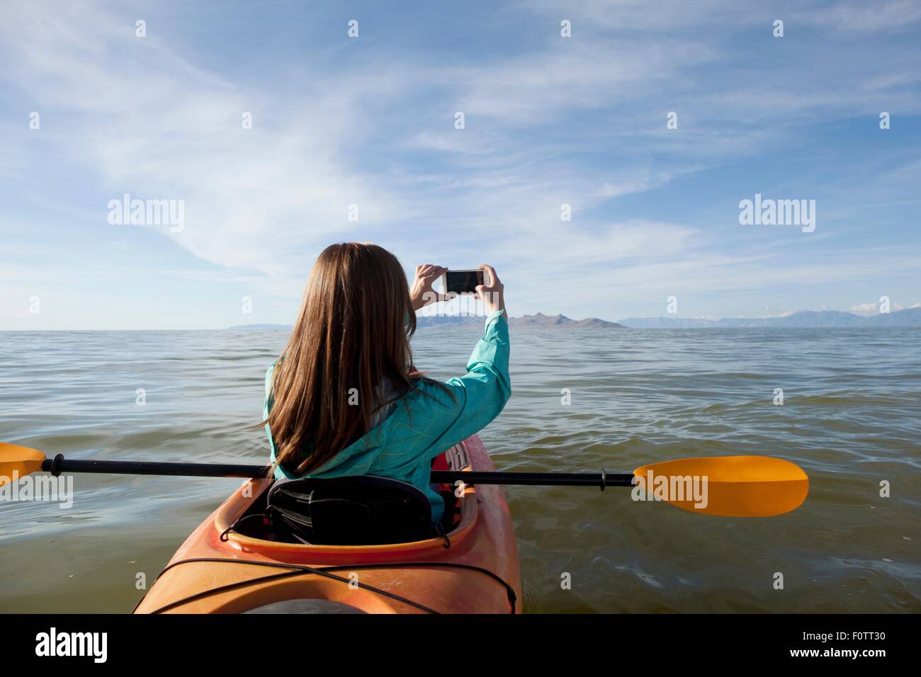 Rear view of young woman in kayak taking photograph, Great Salt Lake, Utah, USA Stock Photo