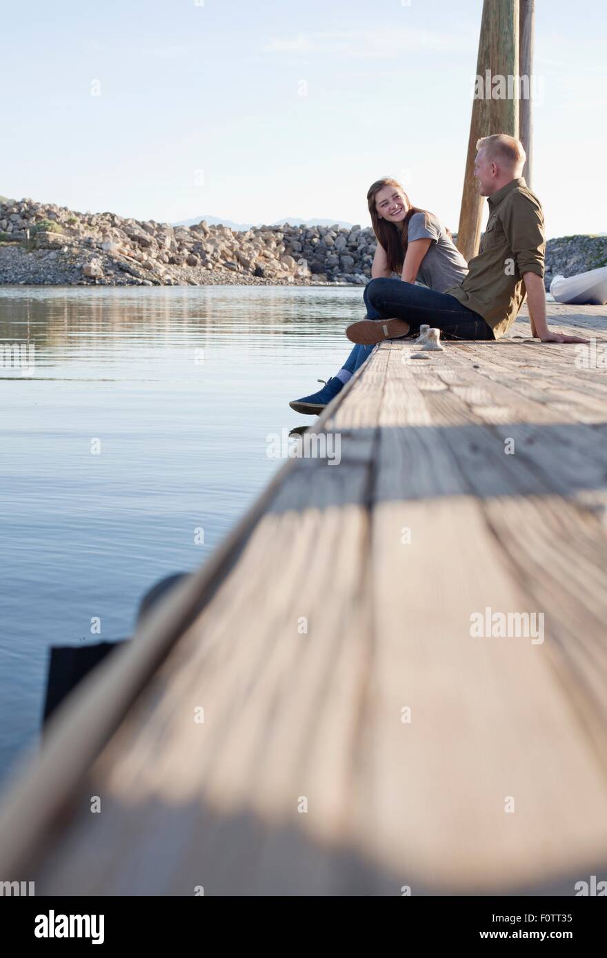 Side view of young couple sitting on wooden pier talking, Great Salt Lake, Utah, USA Stock Photo