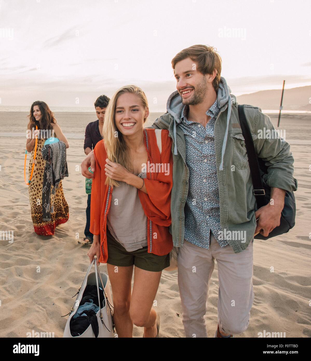 Group of friends walking along beach, young couple looking at smartphone Stock Photo
