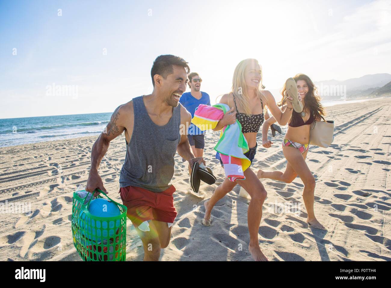 Group of friends running on beach, laughing Stock Photo