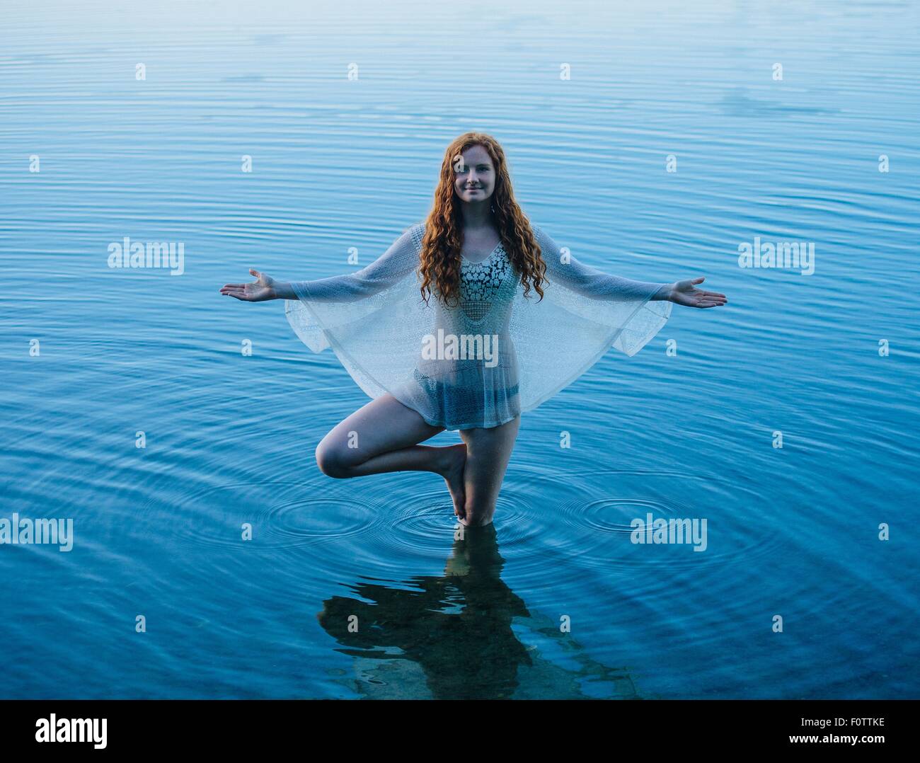 Young woman standing in blue lake practicing yoga Stock Photo - Alamy