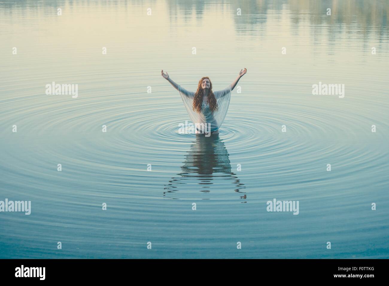 Young woman standing in middle of lake ripples with arms open Stock Photo