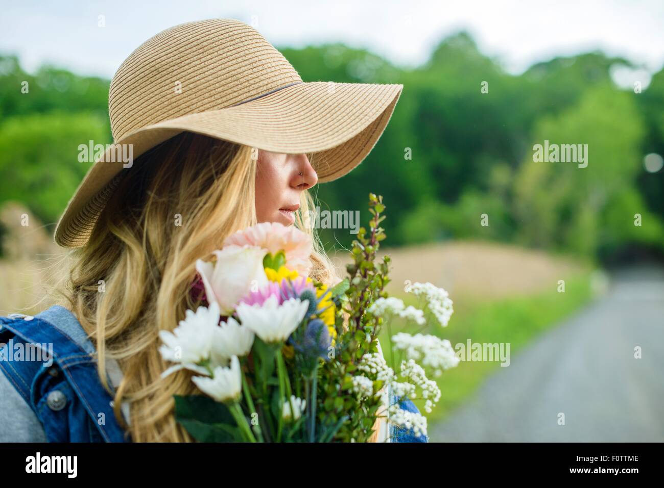 Portrait of young woman with bunch of flowers and wearing straw hat Stock Photo