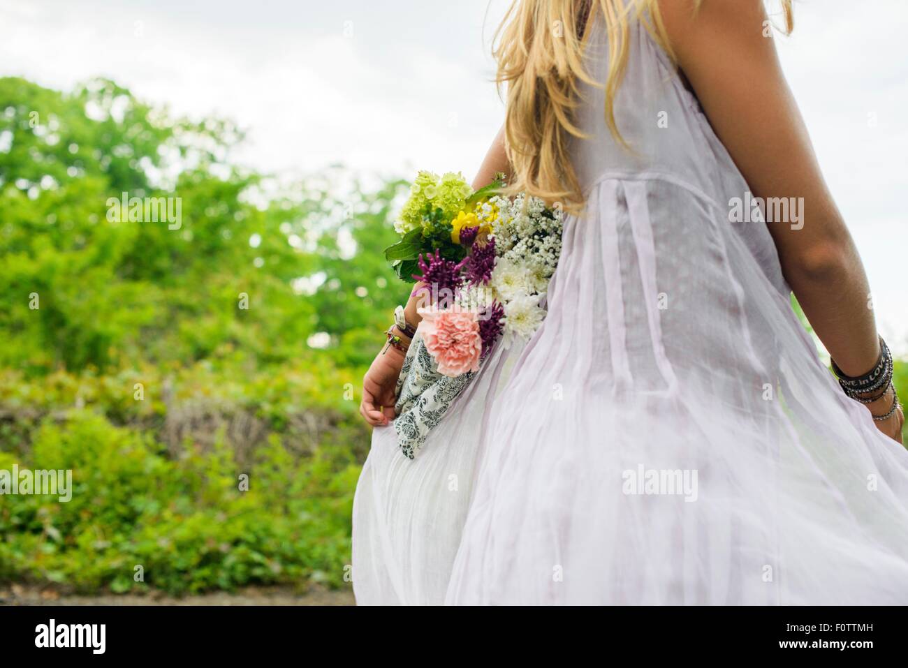 Cropped shot of young woman wearing white dress carrying bunch of flowers behind her back Stock Photo