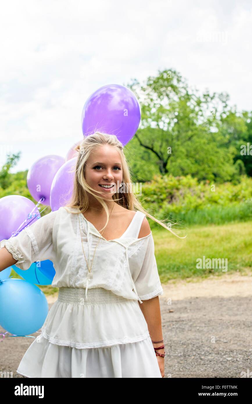 Portrait of pretty young woman with bunch of balloons on rural road Stock Photo