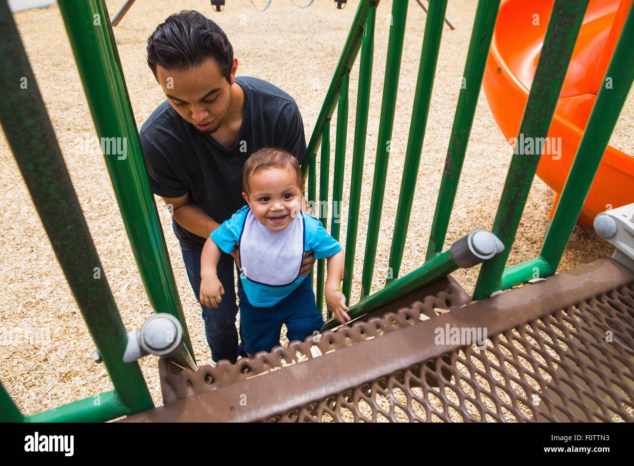 Young man guiding toddler brother up playground slide steps Stock Photo