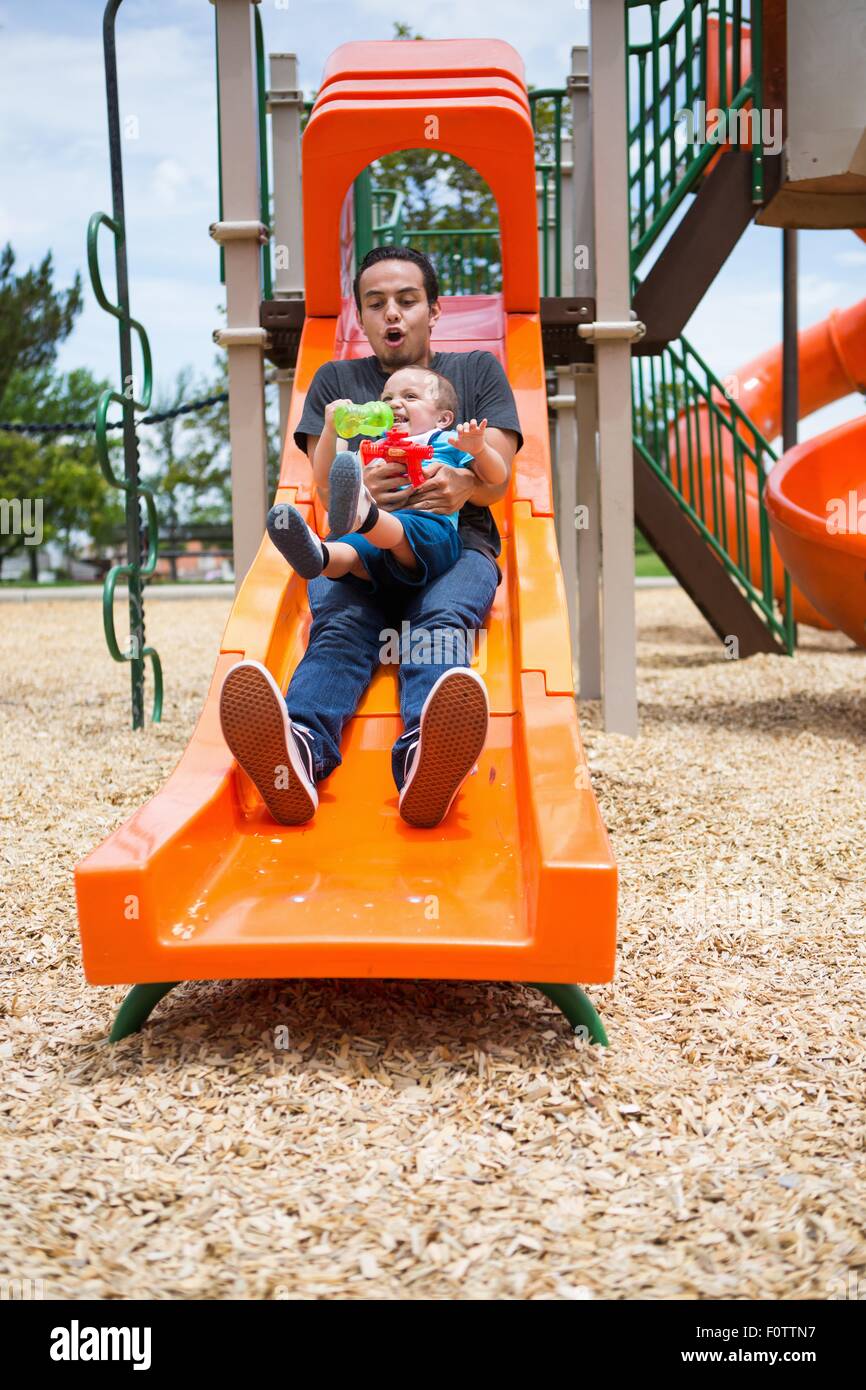 Young man sliding down with toddler brother on playground slide Stock Photo