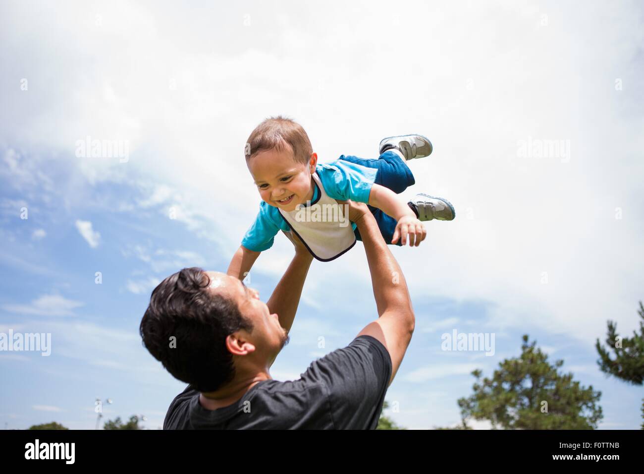 Young man playing lifting up toddler brother in park Stock Photo