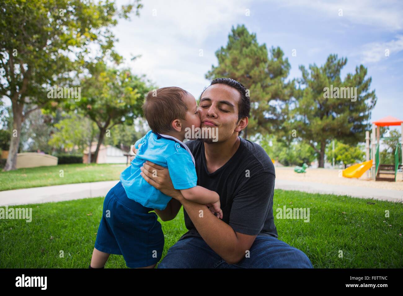 Male toddler kissing older adult brother in park Stock Photo
