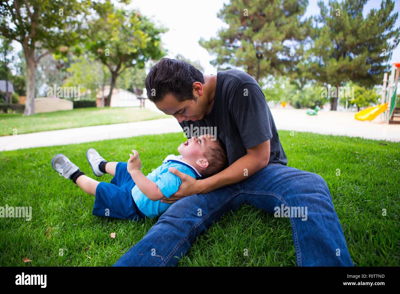 Male toddler playing with older adult brother in park Stock Photo