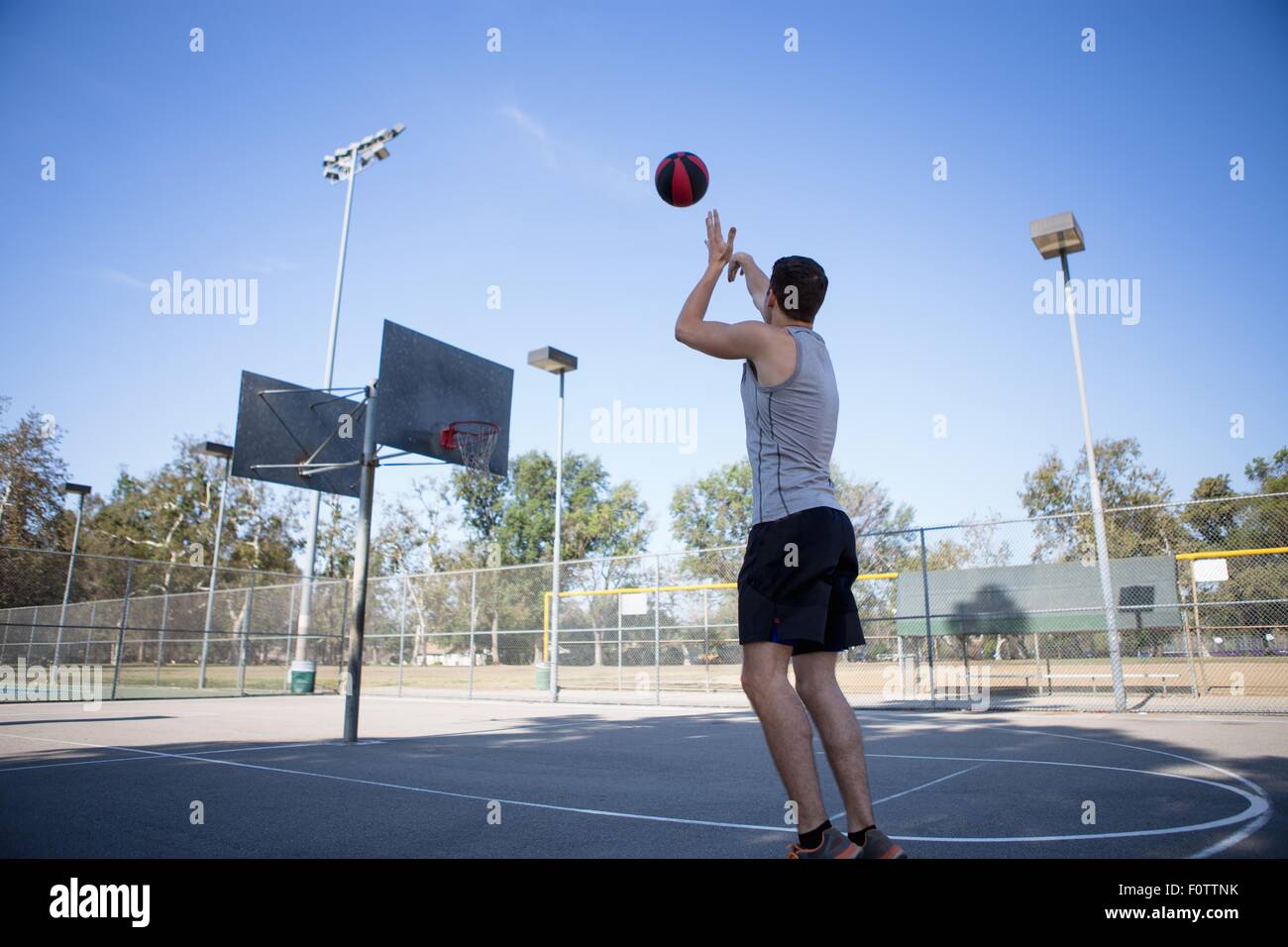 Young male basketball player throwing ball toward basketball hoop Stock