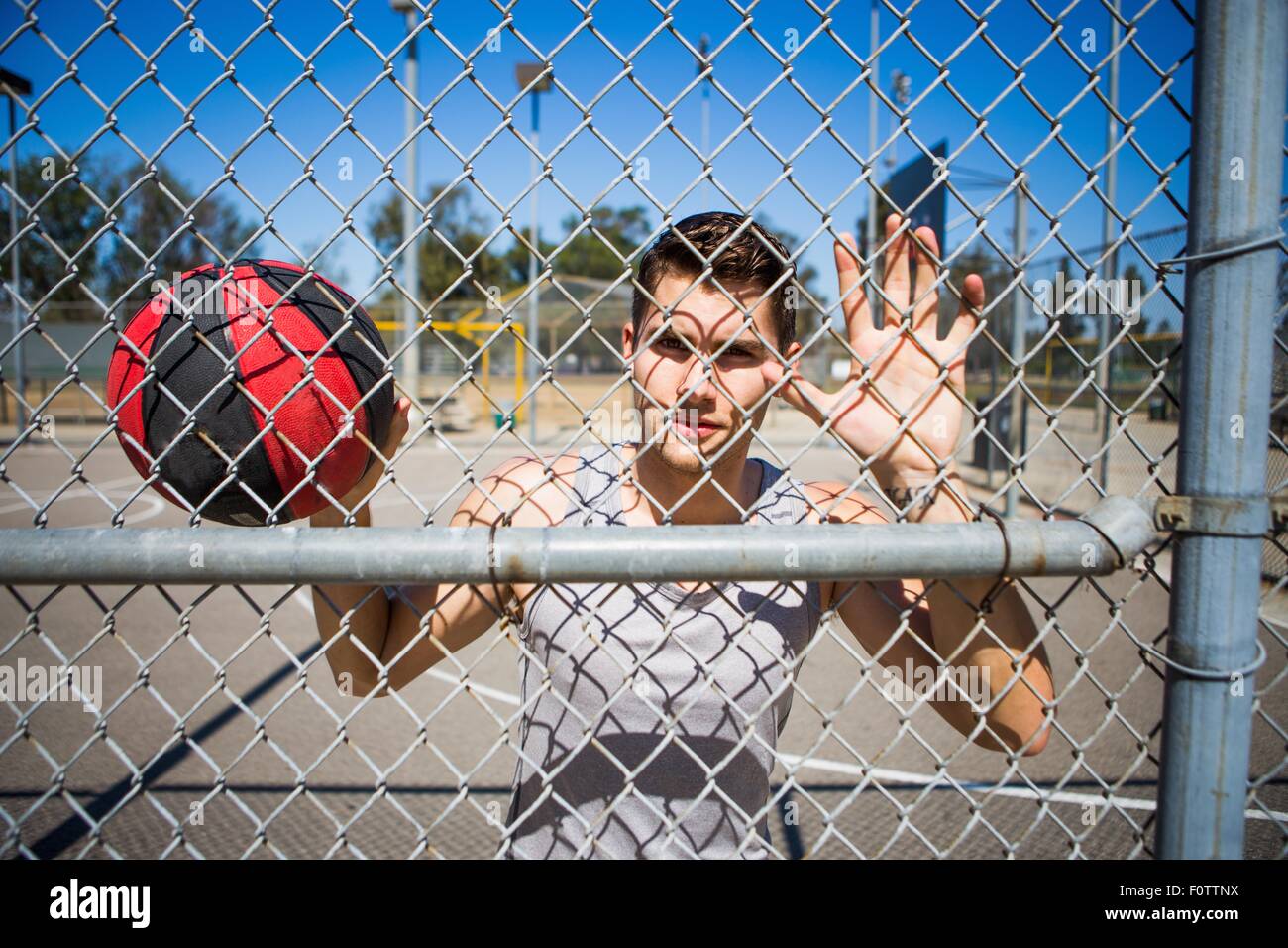 Portrait of young male basketball player behind basketball court fence