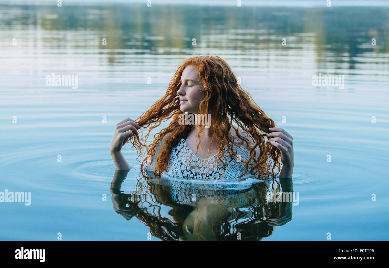 Head and shoulders of beautiful young woman with long red hair in lake Stock Photo