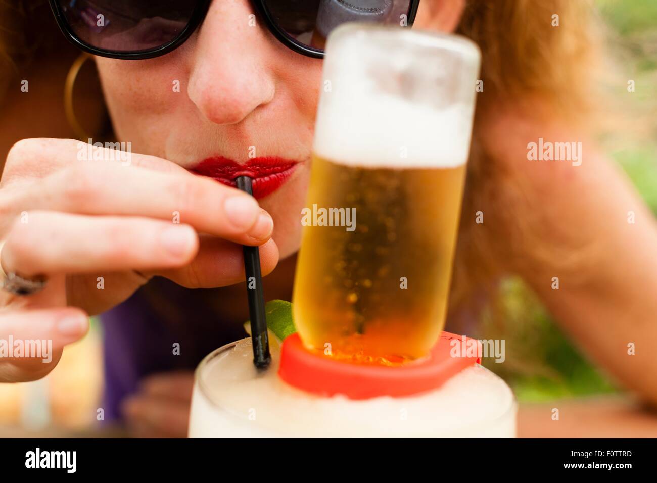 Close up of mid adult woman drinking beer with drinking straw Stock Photo