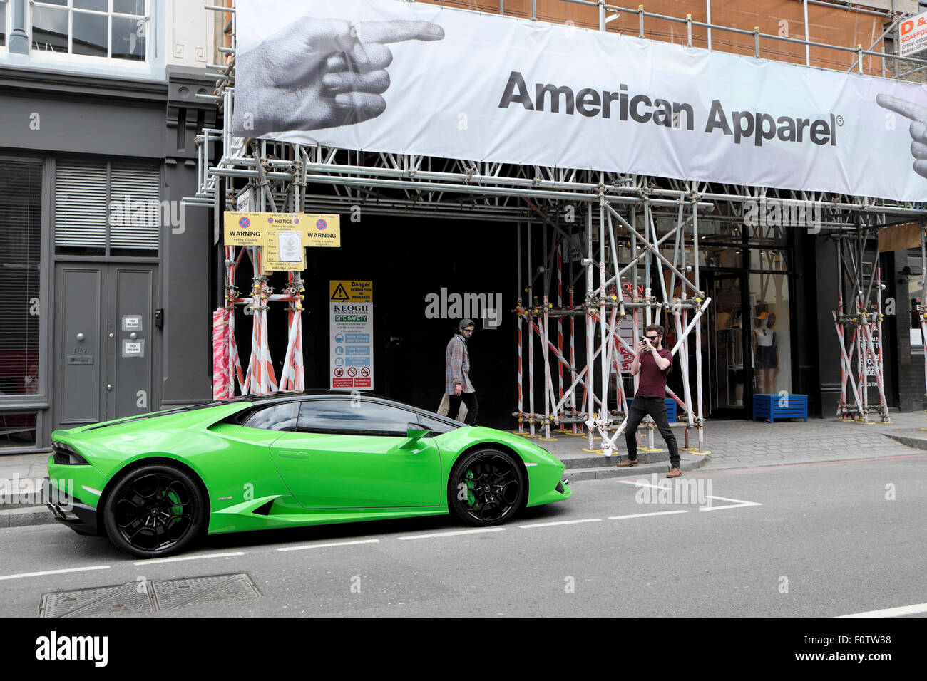 Man photographing green Lamborghini parked outside American Apparel shop in Shoreditch East London, UK   KATHY DEWITT Stock Photo