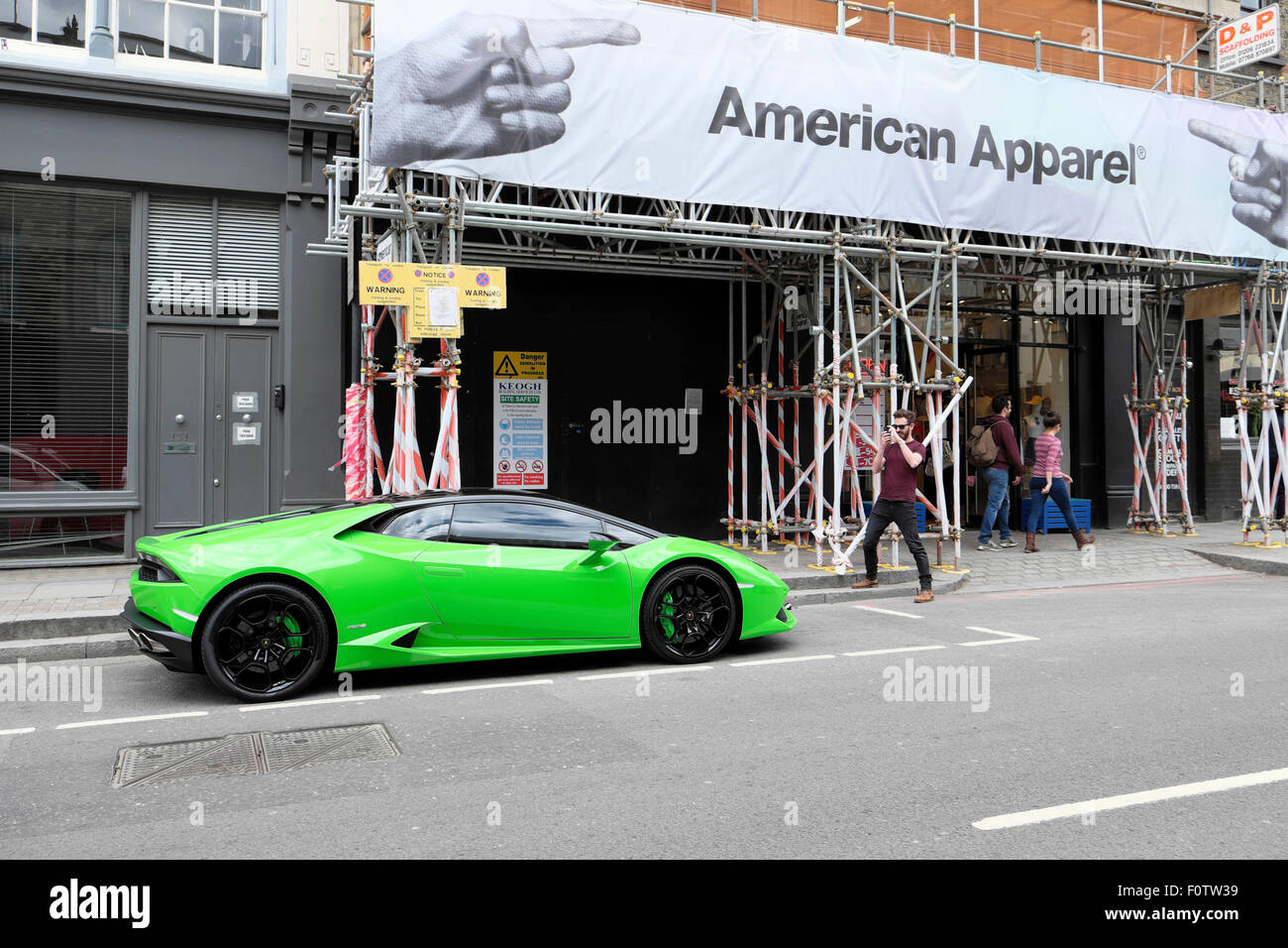 Man photographing green Lamborghini parked outside American Apparel shop in Shoreditch East London, UK   KATHY DEWITT Stock Photo