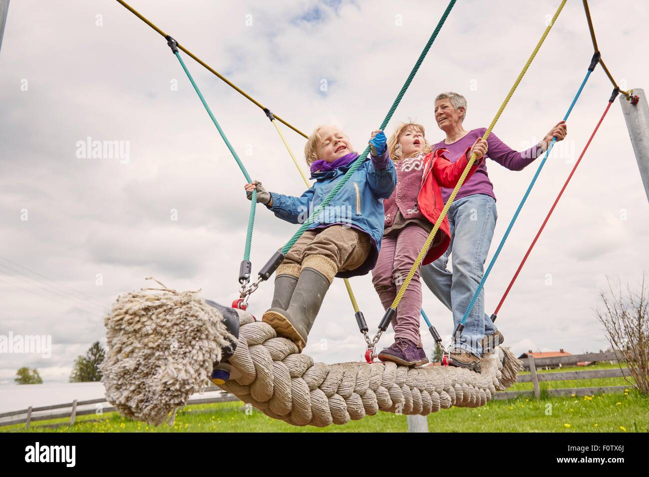 Grandmother and grandchildren playing on rope bridge, low angle view Stock Photo