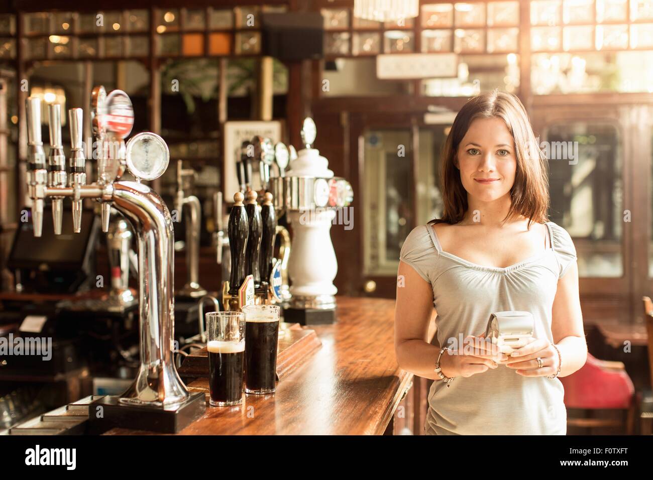Mid adult woman working in public house holding chip and pin machine Stock Photo
