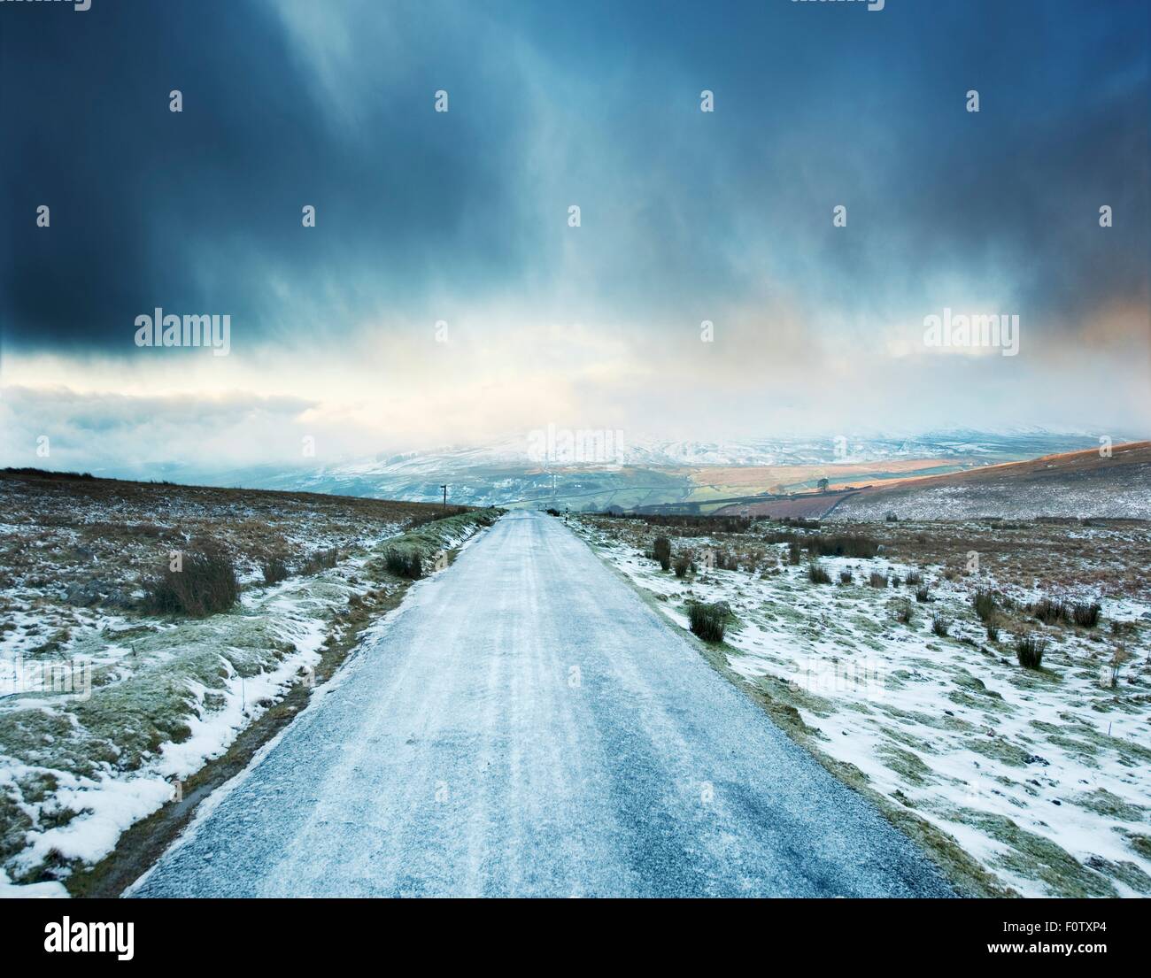 Icy rural road with storm clouds ahead, Swaledale, Yorkshire, UK Stock Photo