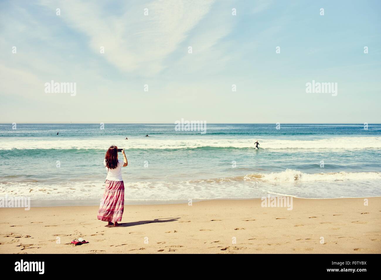 Rear view of woman on beach taking photograph of the ocean, Venice ...