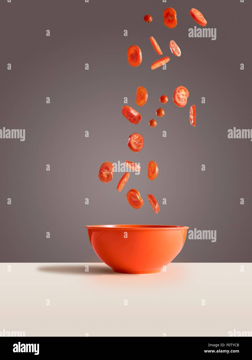 Fresh sliced tomatoes dropping into red bowl Stock Photo