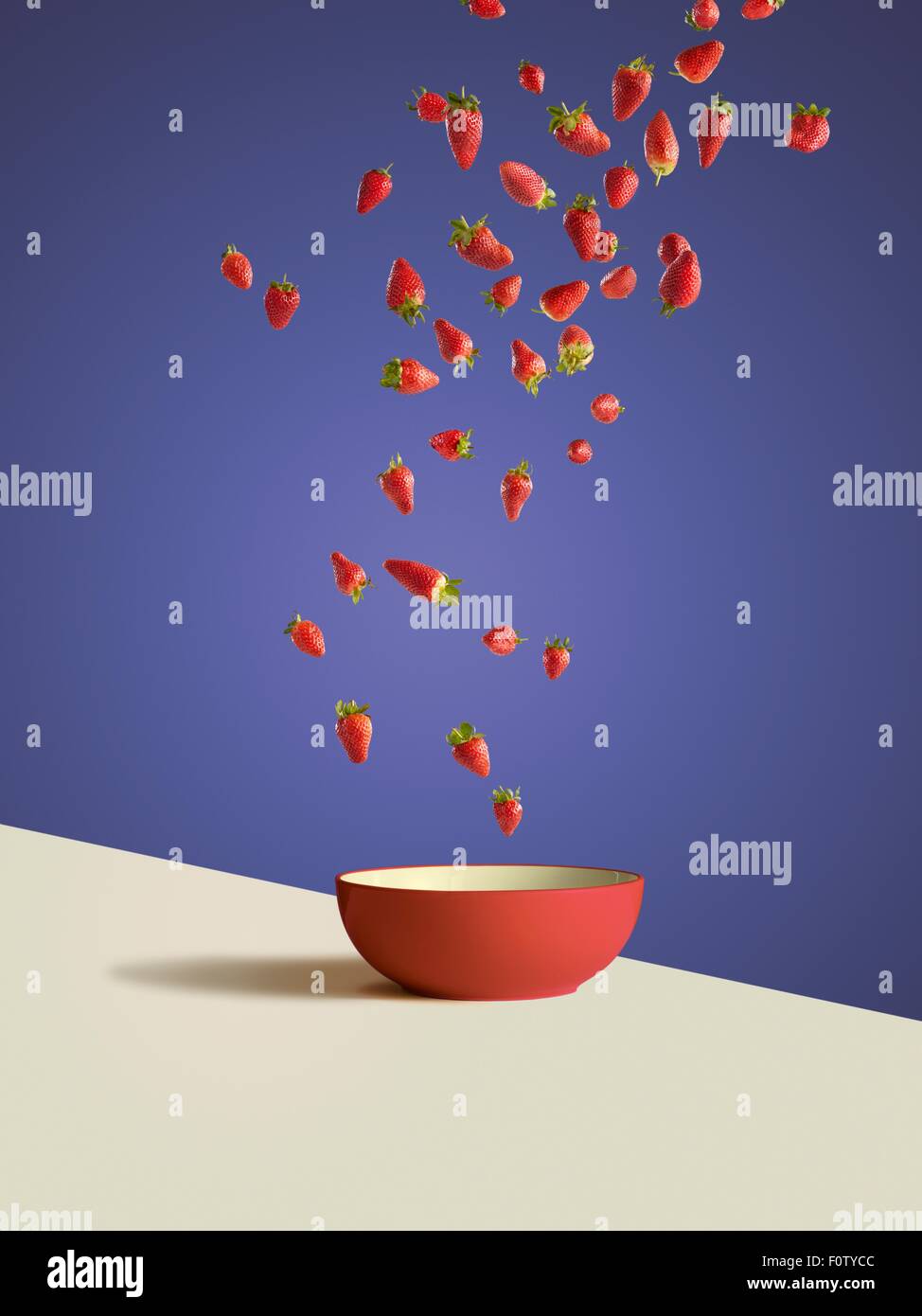 Fresh sliced strawberries dropping into red bowl Stock Photo