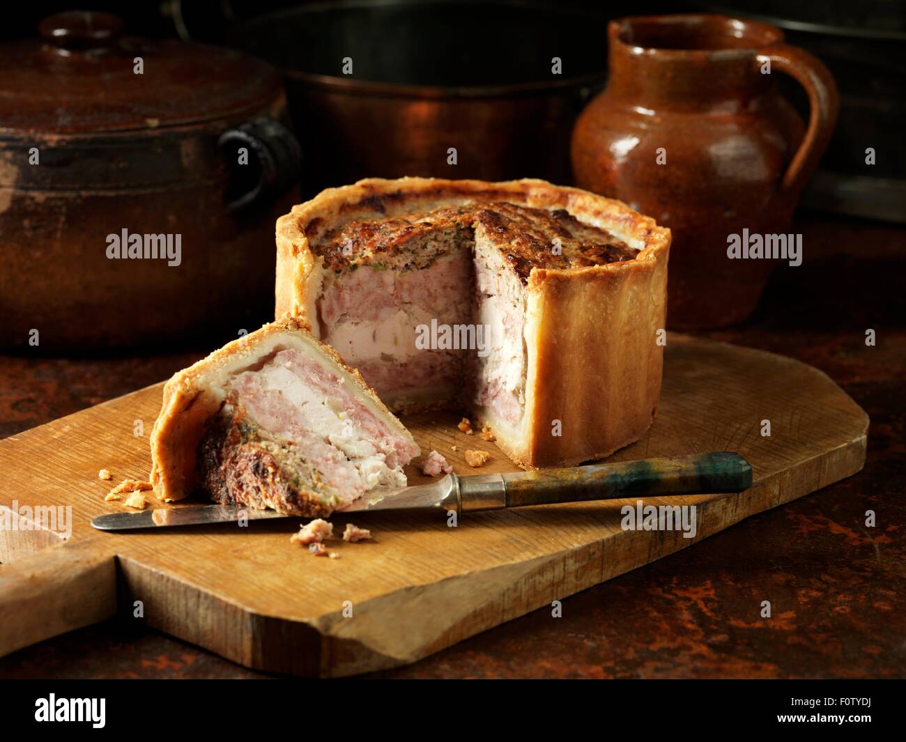 Rustic still life with layered pork, chicken and stuffing pie on chopping board Stock Photo