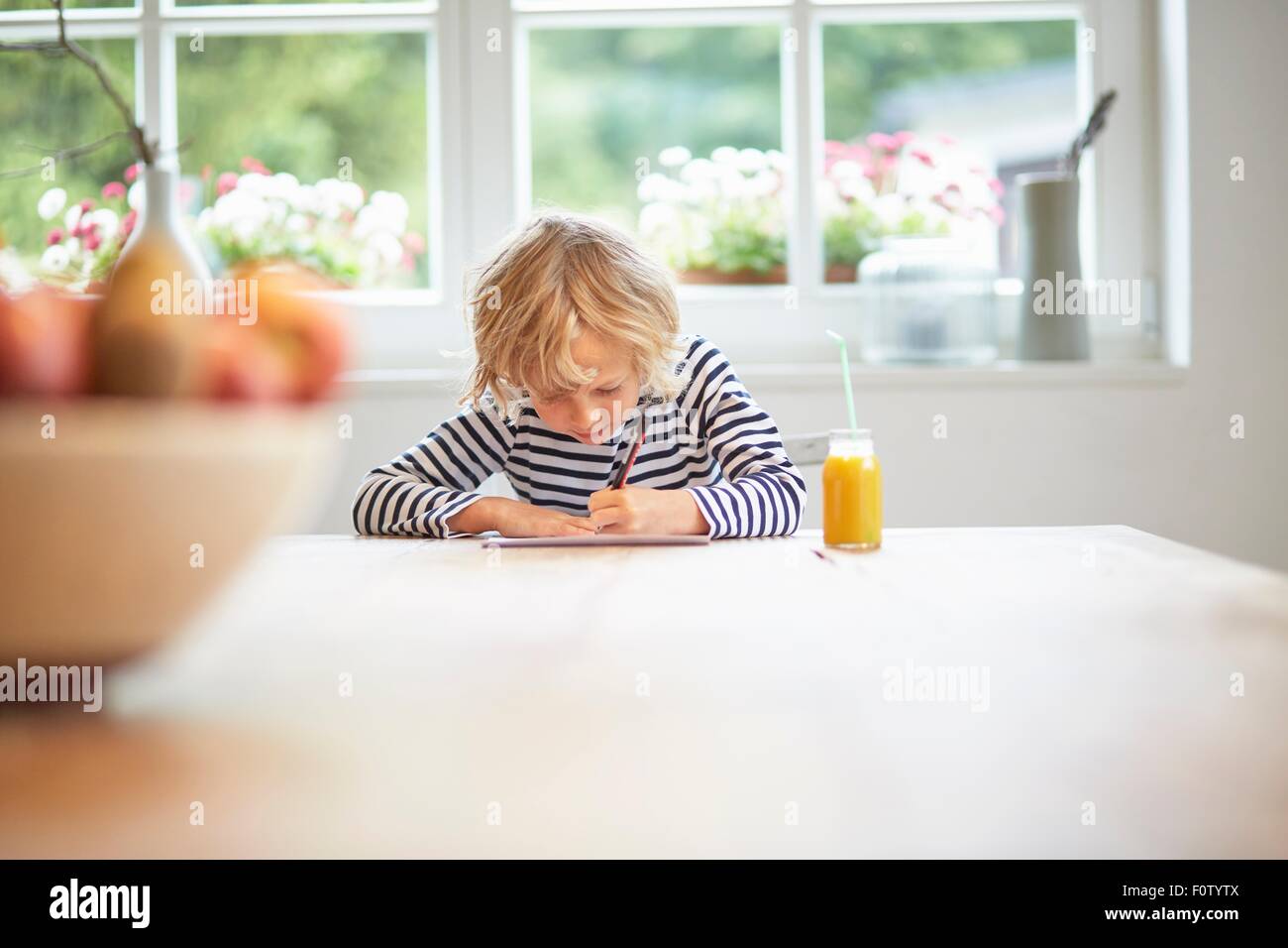 Young boy sitting at table drawing on paper Stock Photo