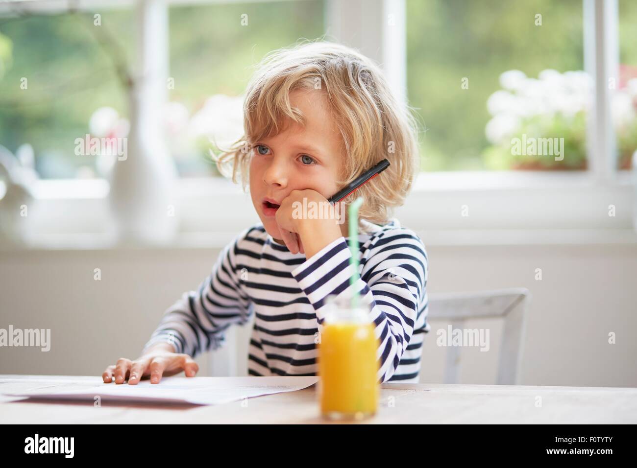 Young boy sitting at table holding pen, thinking Stock Photo