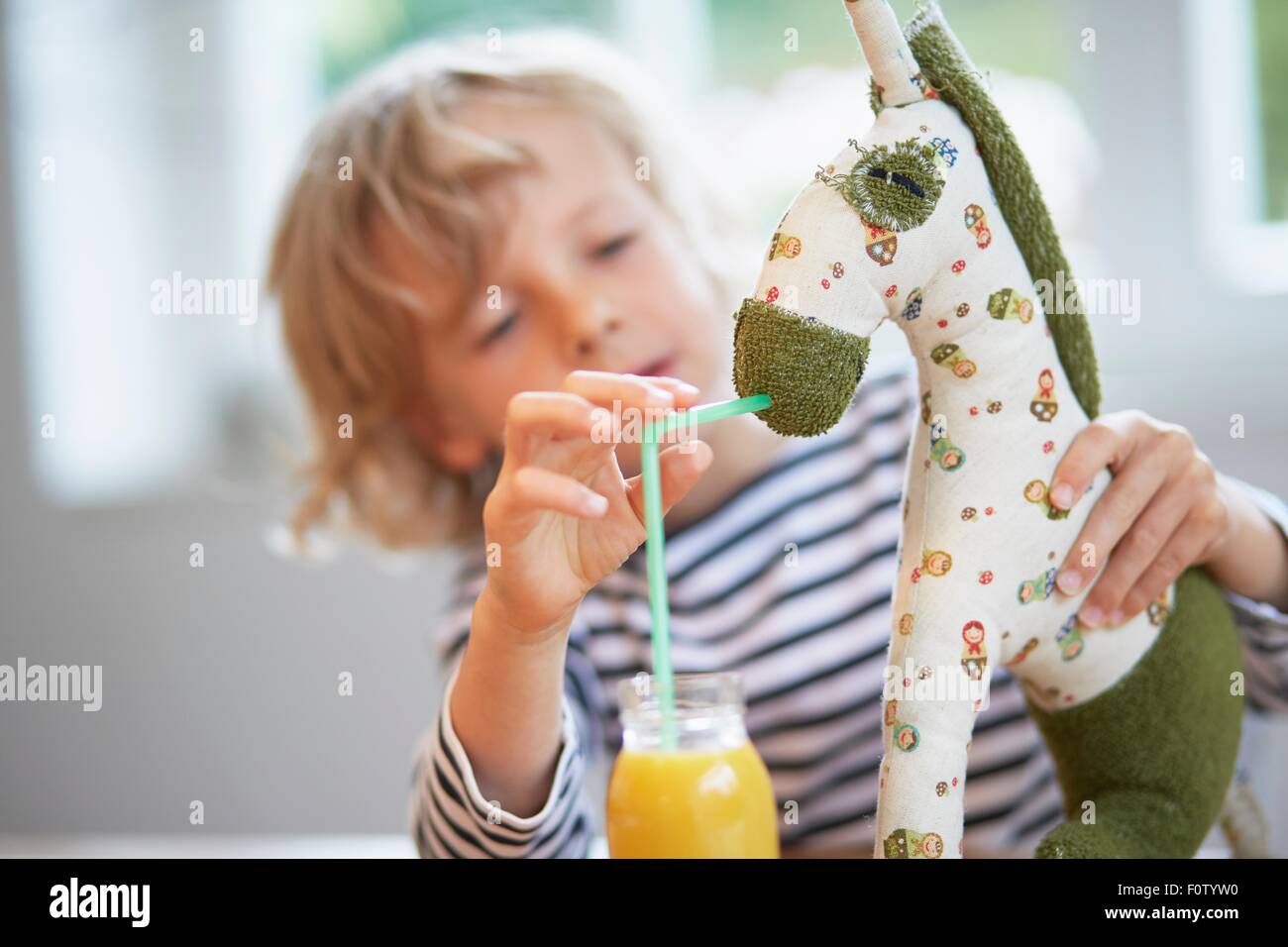 Young boy pretending to feed drink to soft toy Stock Photo