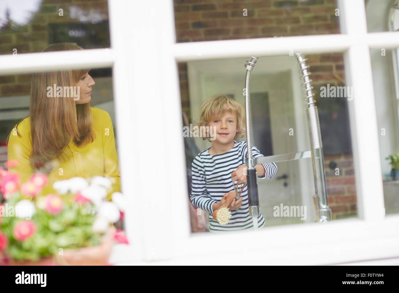 Mother and son doing washing up, view through window Stock Photo