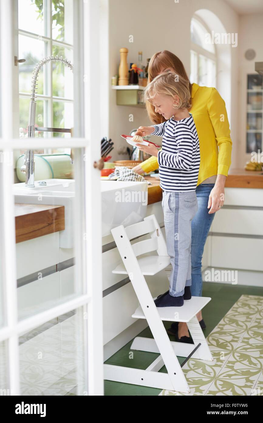 Mother and son doing washing up, young boy standing on chair Stock Photo