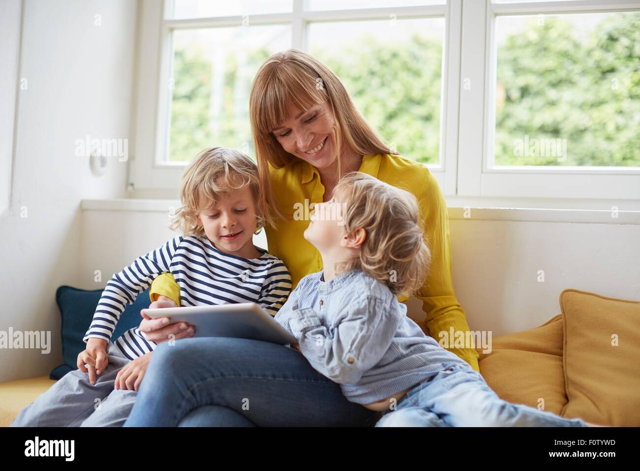 Mother and two sons, sitting in window seat, looking at digital tablet Stock Photo