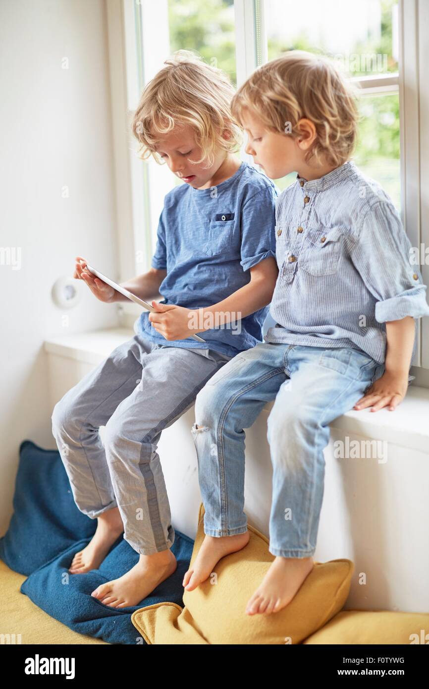 Two young brothers, sitting in window seat, looking at digital tablet Stock Photo