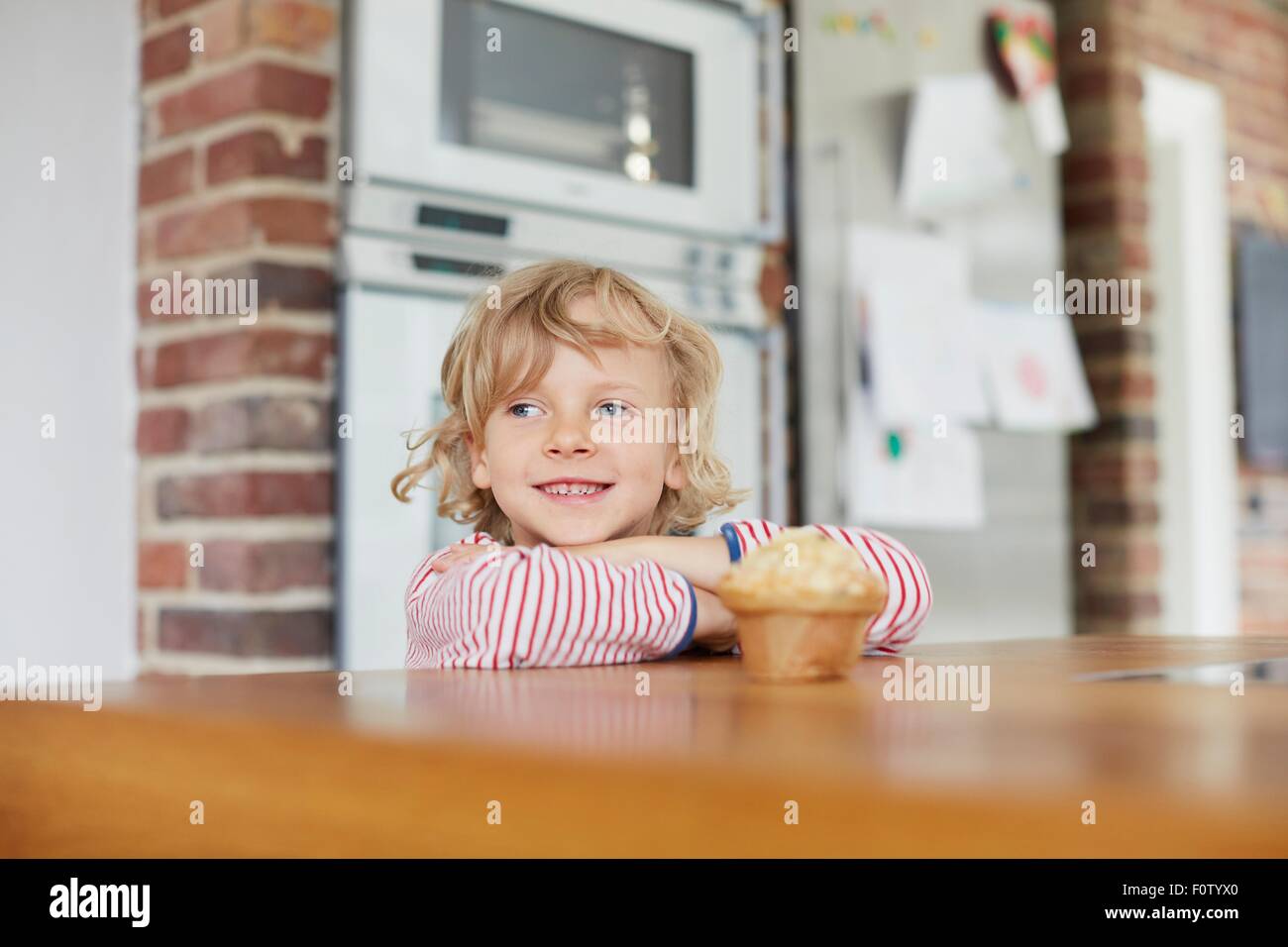 Young boy standing by kitchen counter,with muffin on counter in front of him Stock Photo