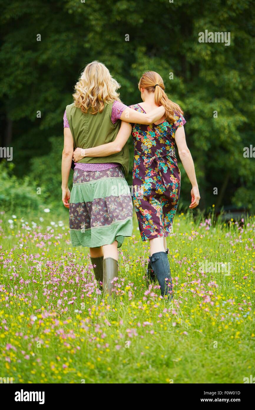 Rear view of two women walking in wildflower meadow Stock Photo
