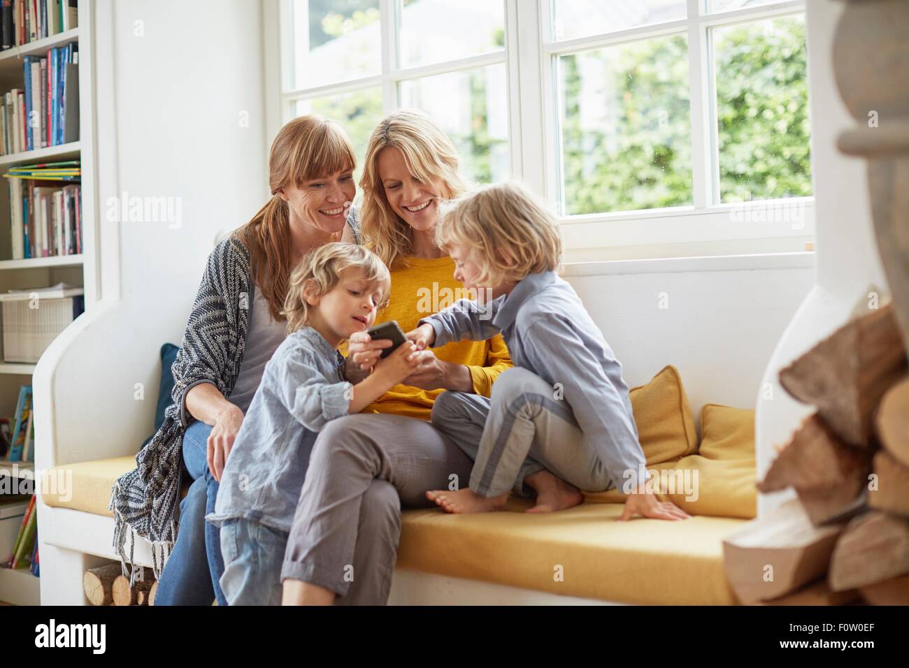 Adult women and boys sitting on window seat looking at smartphone Stock Photo