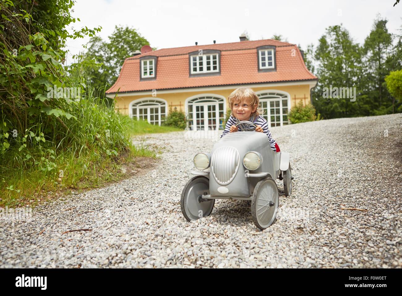 Boy playing with vintage toy car on driveway in front of house Stock Photo