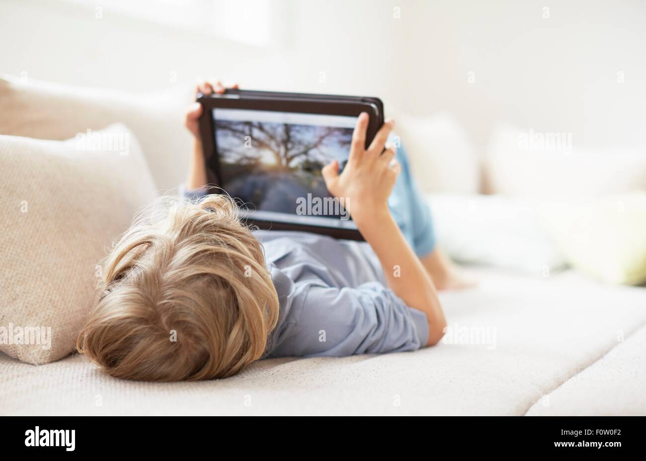 Boy lying on back on sofa using digital tablet Stock Photo