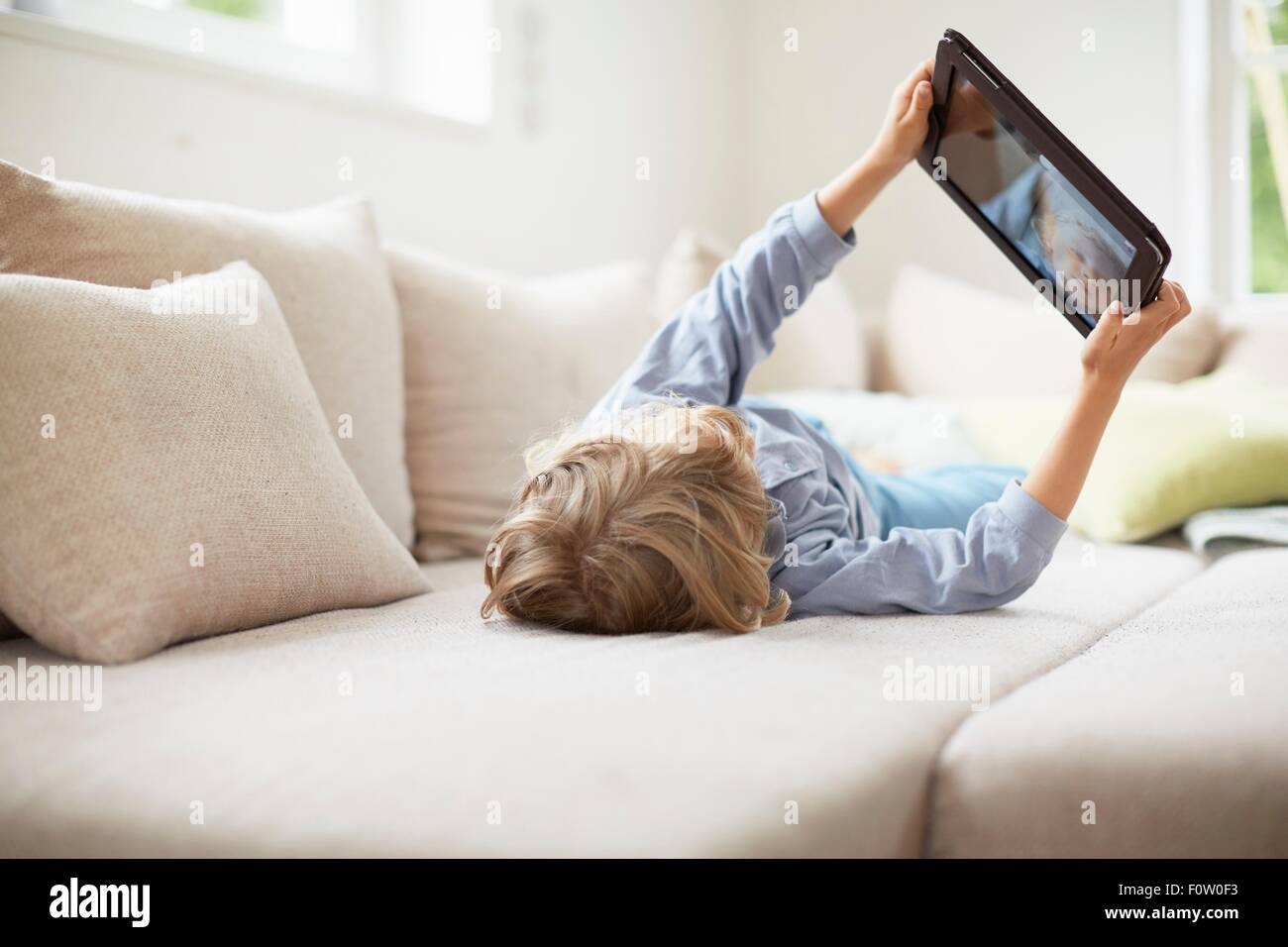 Boy lying on back on sofa using digital tablet, arms raised Stock Photo ...