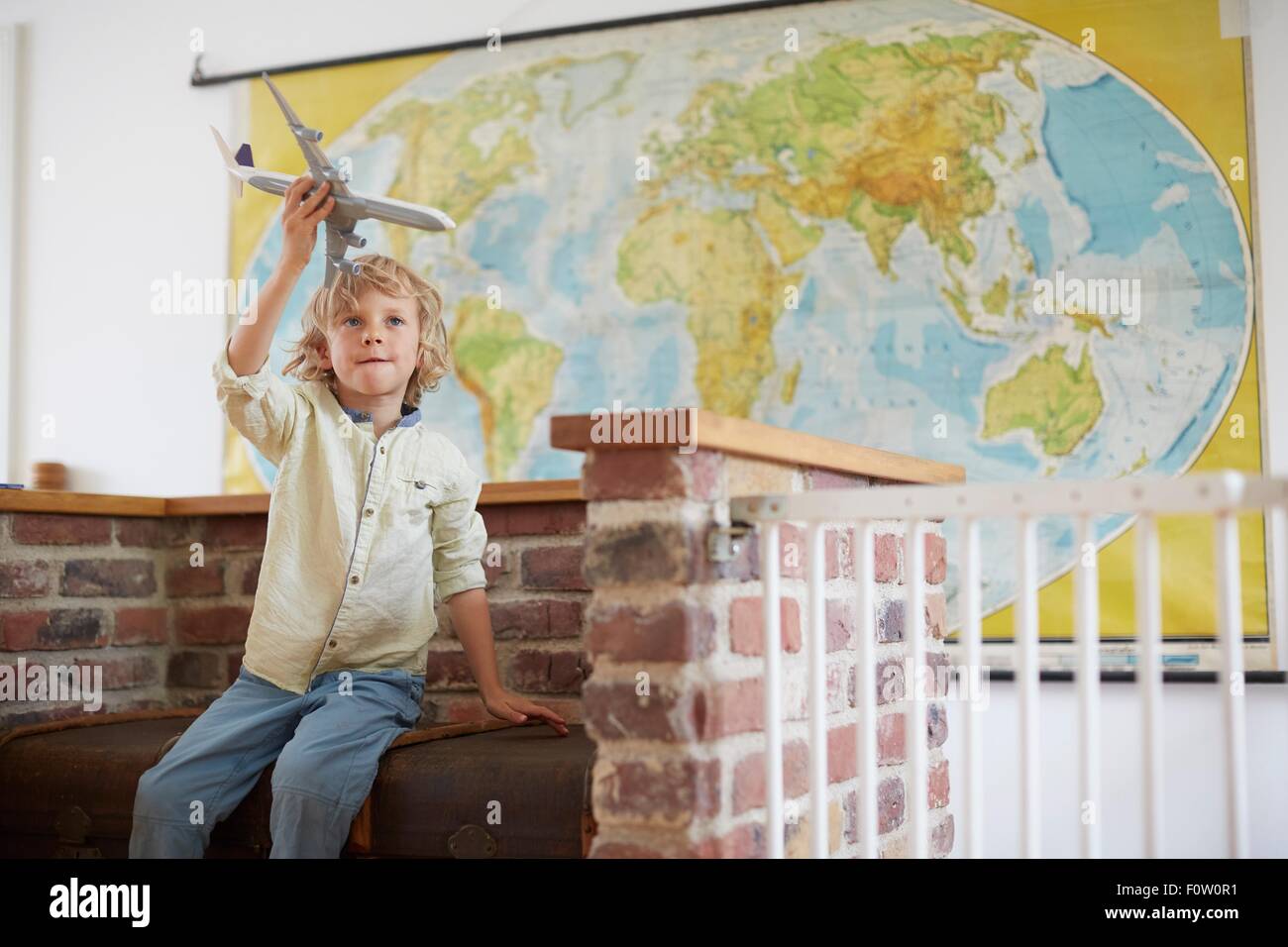 Boy sitting in front of world map playing with toy aeroplane Stock Photo