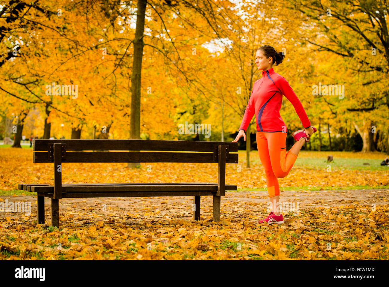 Young woman warming up at bench before jogging in autumn nature Stock Photo