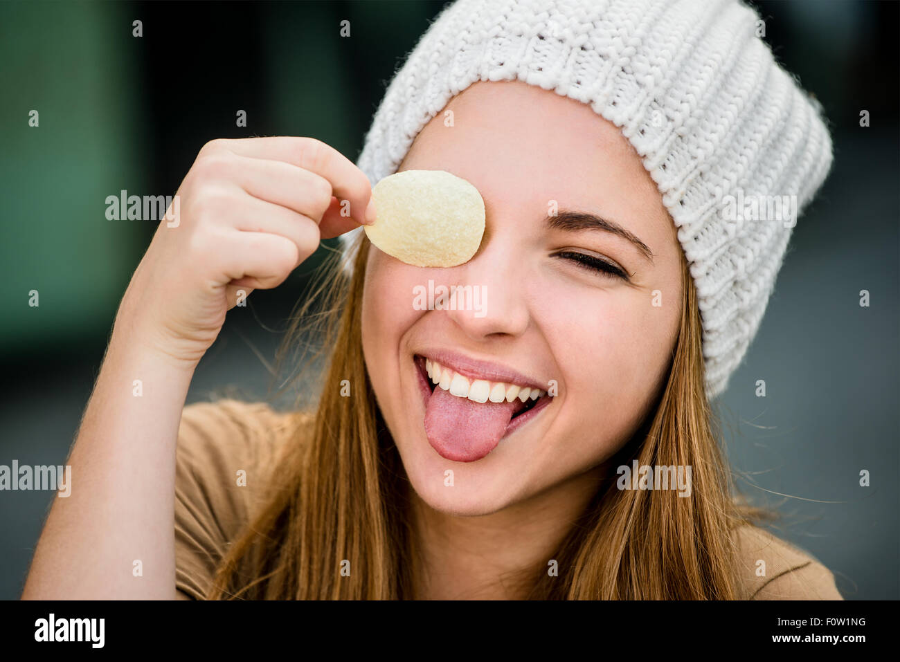 Teenager girl in cap having fun with potato chips on eyes outdoor in street Stock Photo
